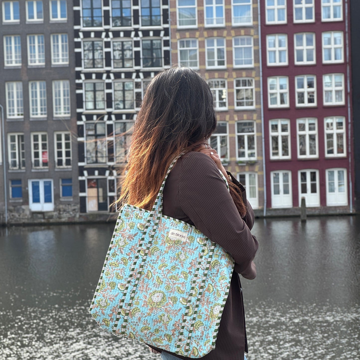 Person with a patterned bag standing by a canal with historic buildings in the background