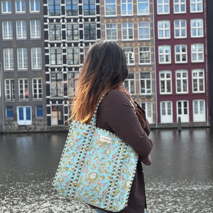 Person with a patterned bag standing by a canal with historic buildings in the background