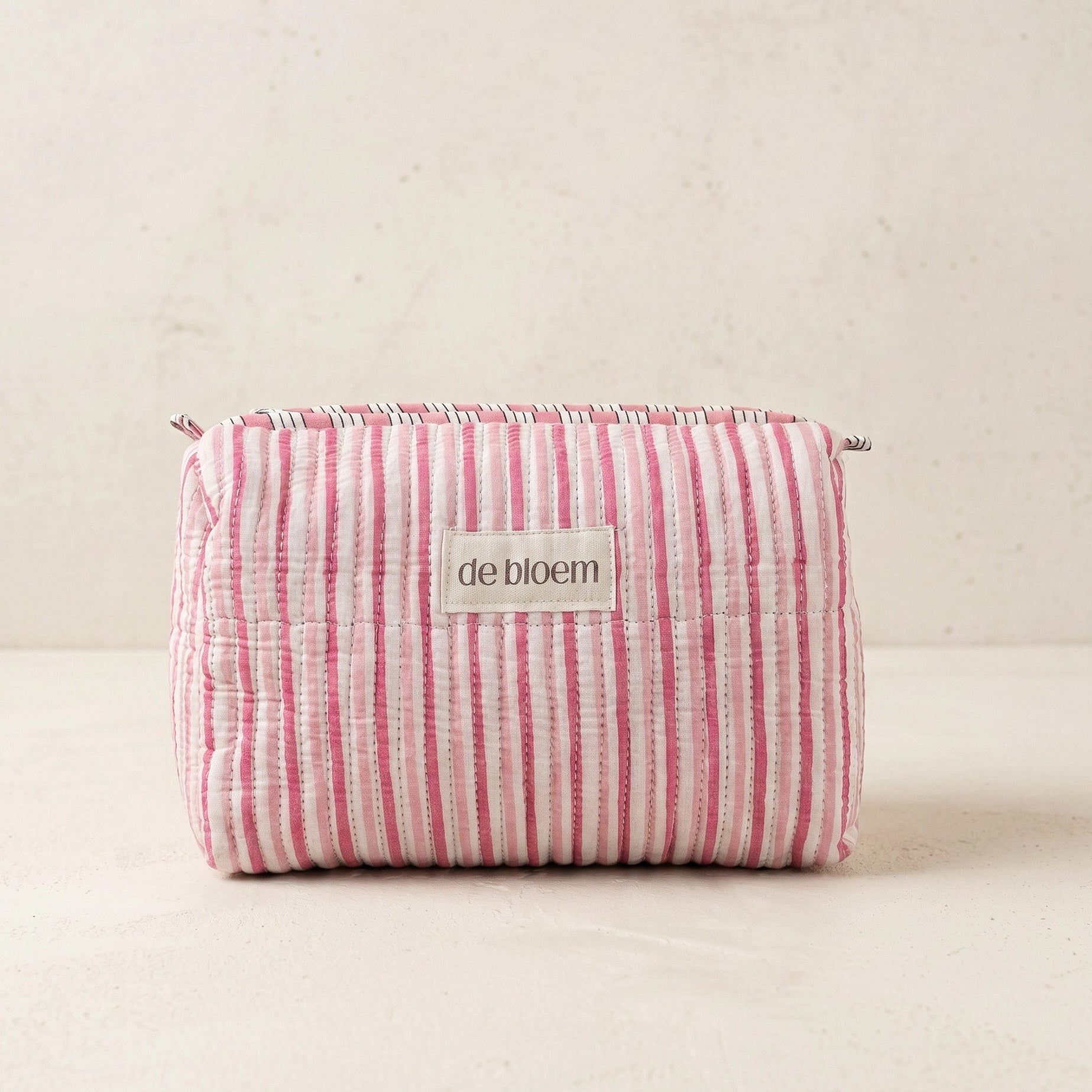Pink and white striped pouch with 'de bloem' label on a beige background