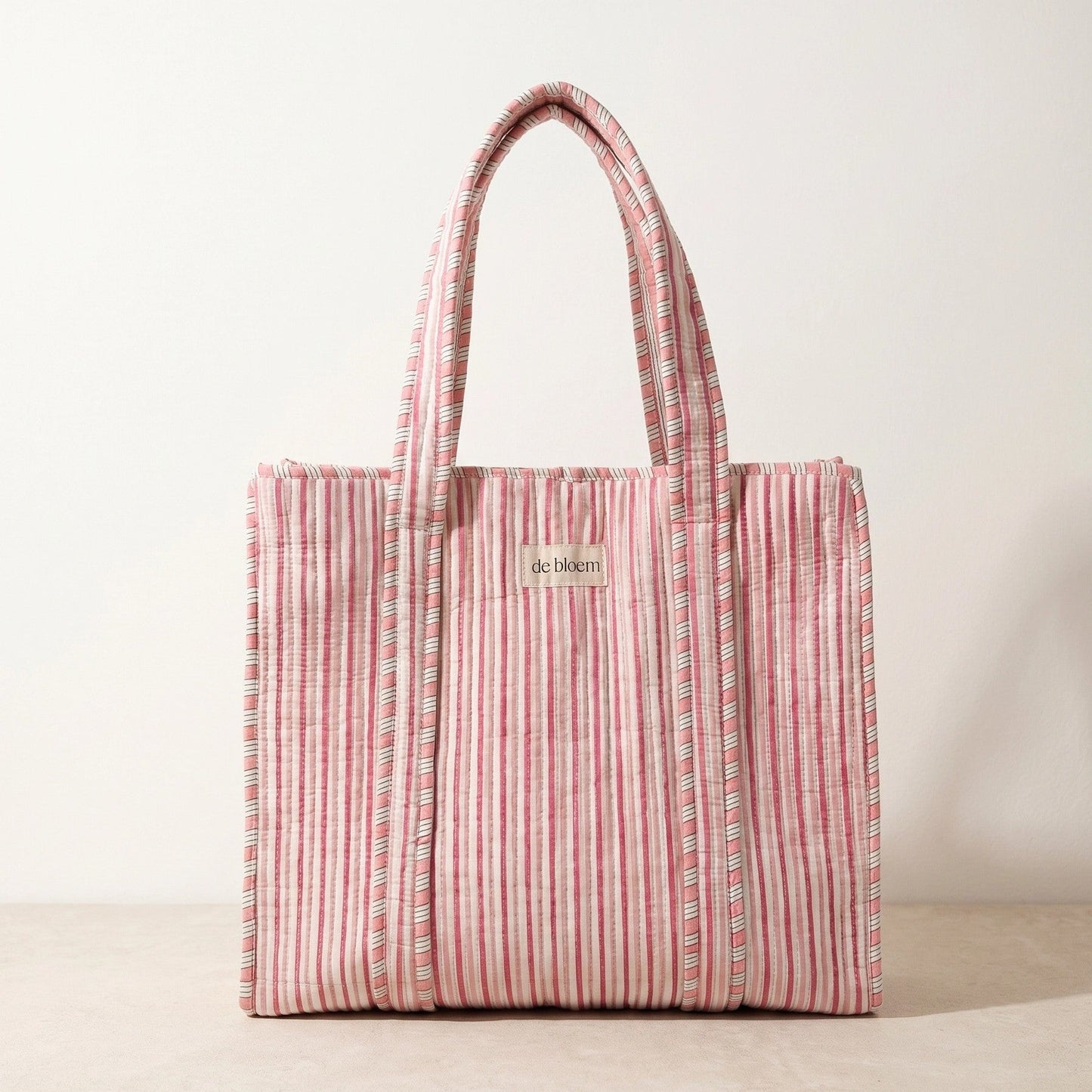 Handmade pink striped quilted cosmetic pouch with a yellow and blue floral print and de bloem logo label.
