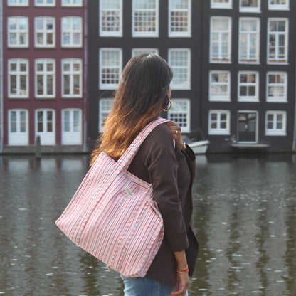 Woman with a pink bag standing by a canal with traditional Dutch houses.