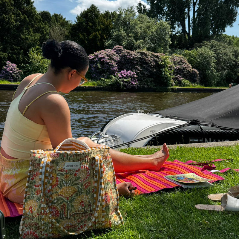 Woman sitting on a colorful blanket by a river with a bag next to her