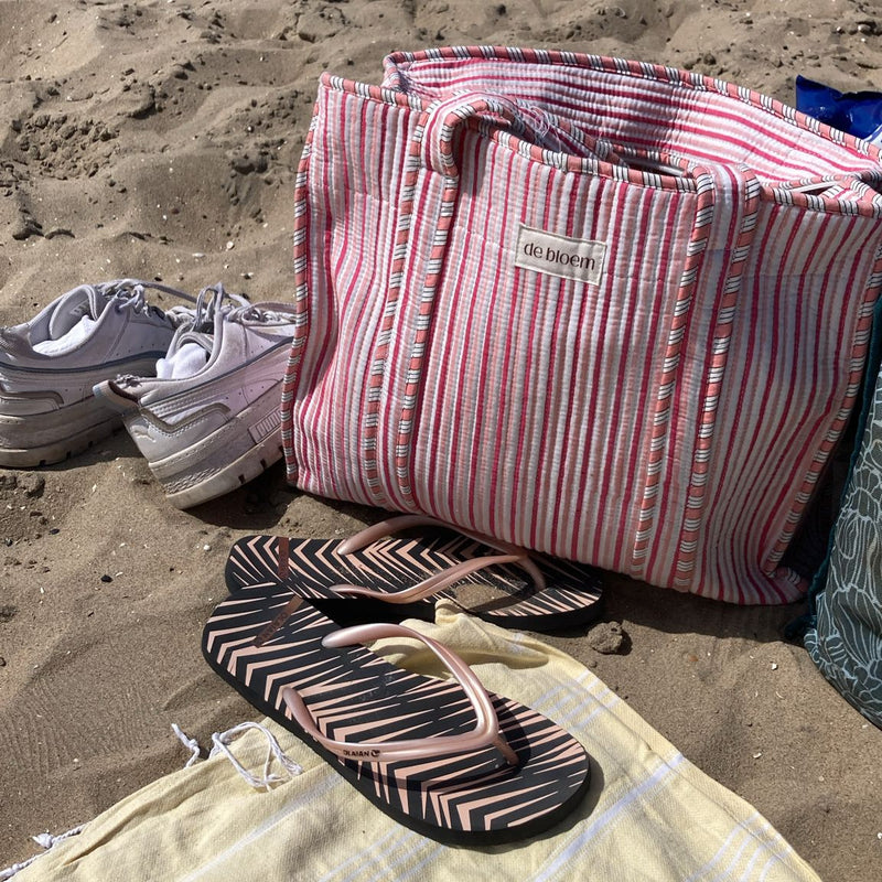 Striped beach bag, flip-flops, and shoes on a sandy beach.