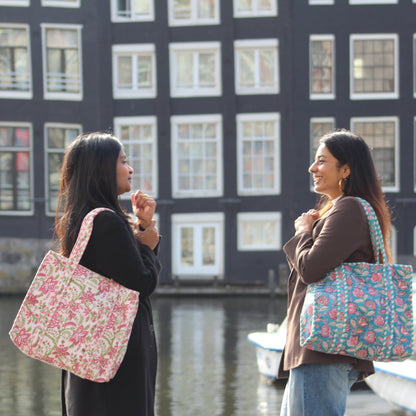 Two women standing by a canal with floral-patterned bags, buildings in the background