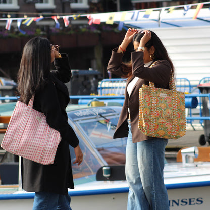Two women with patterned bags standing near boats at a dock.