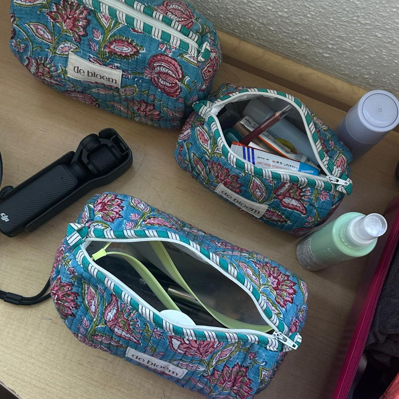 Three floral-patterned makeup bags on a surface with various items around.