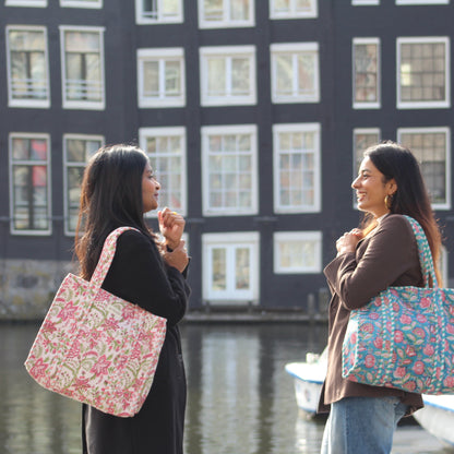 Two women standing by a canal with floral-patterned bags, buildings in the background