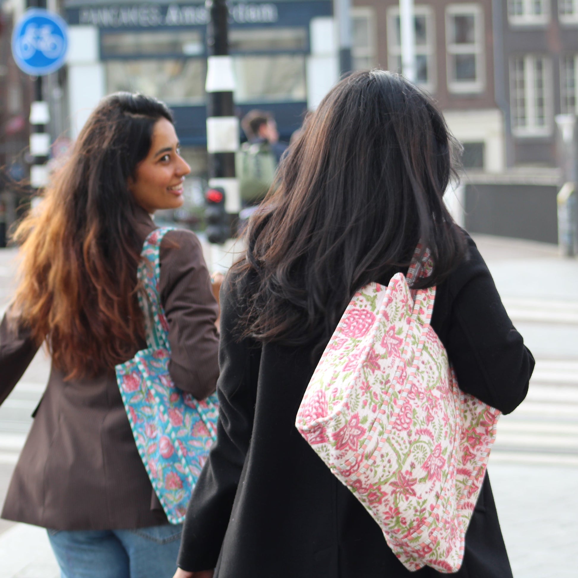 Two women walking outdoors with floral-patterned bags.